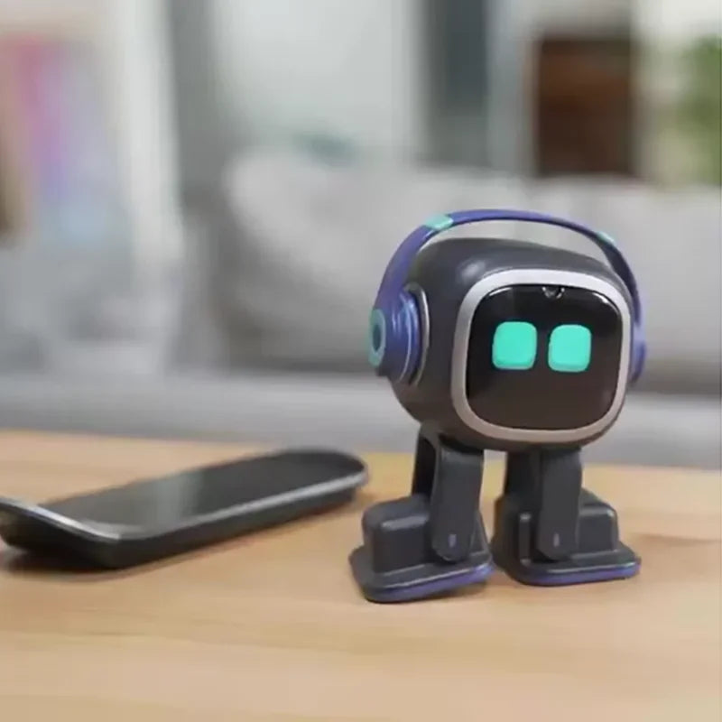 Black desktop robot pet toy with headphones standing on a wooden desk beside a phone