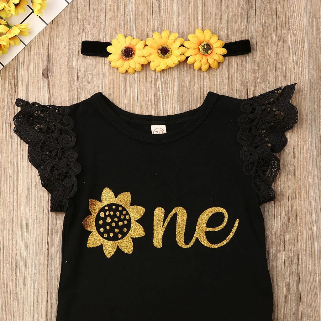 Black outfit with sunflower design and 'one' text, paired with a matching headband on a wooden surface.