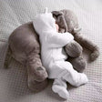 Plush elephant toy and baby in white outfit on a textured surface