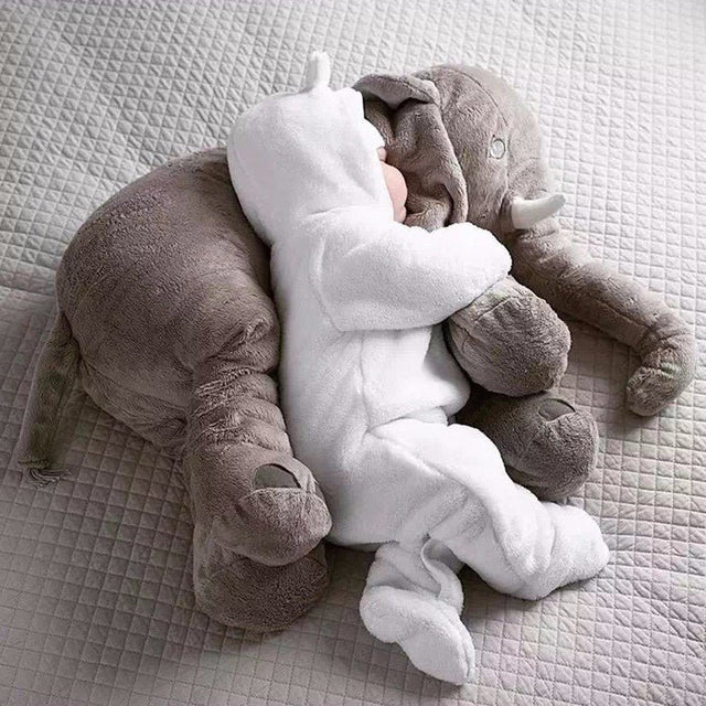Plush elephant toy and baby in white outfit on a textured surface