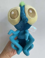 Blue and green plush toy with large eyes held by a hand against a white background