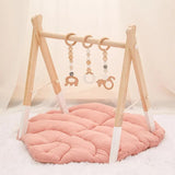 Wooden baby gym with pink mat and hanging toys.