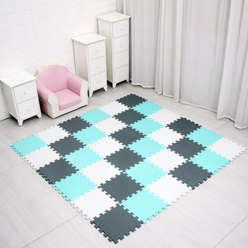 Checkered foam puzzle mat on a floor with white furniture and pink chair.