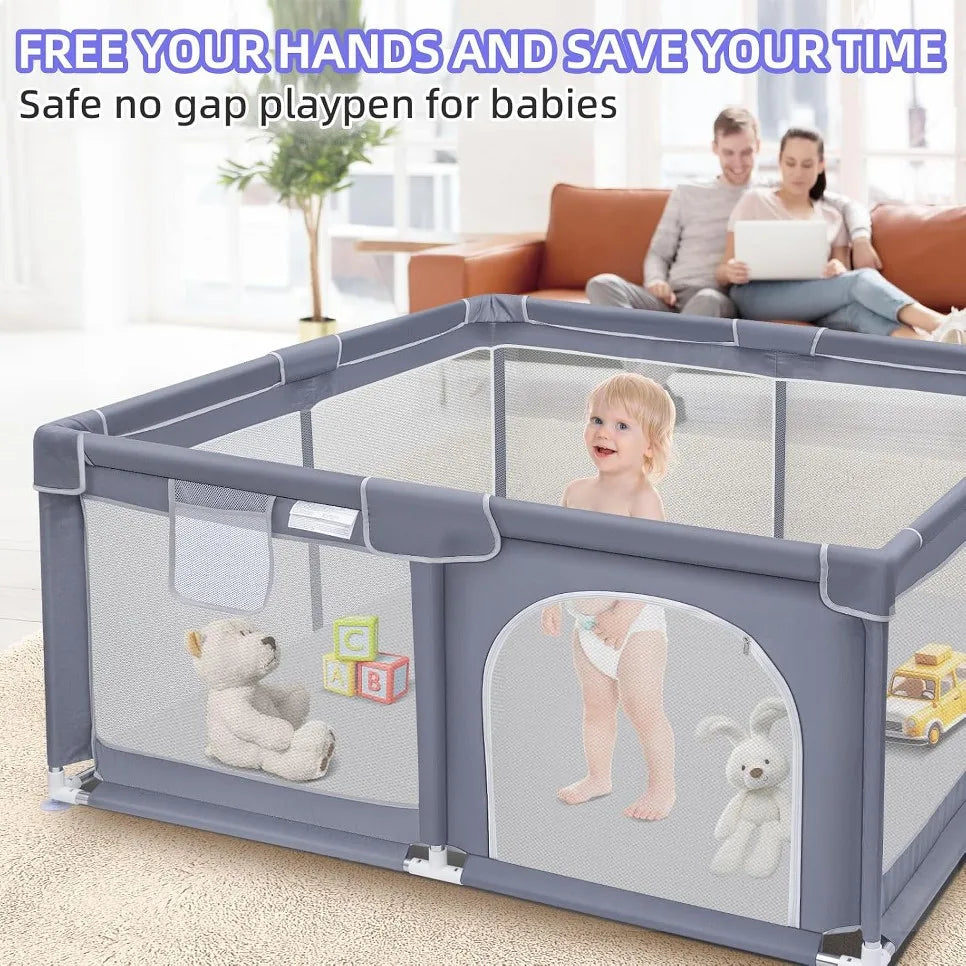 Baby standing in a grey playpen with toys while parents sit on a sofa behind it