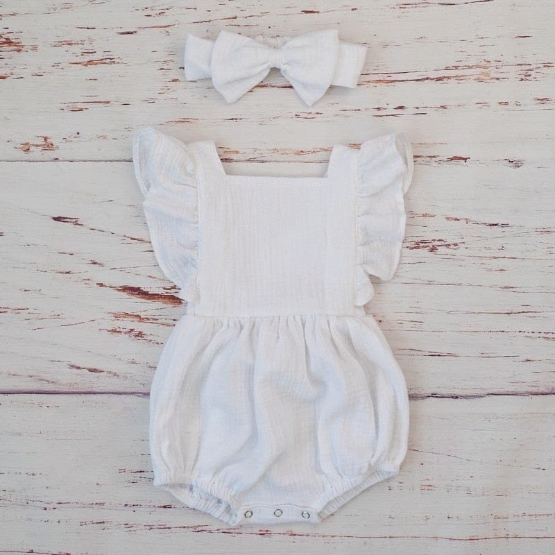 White baby romper with ruffled sleeves and matching headband on a wooden surface