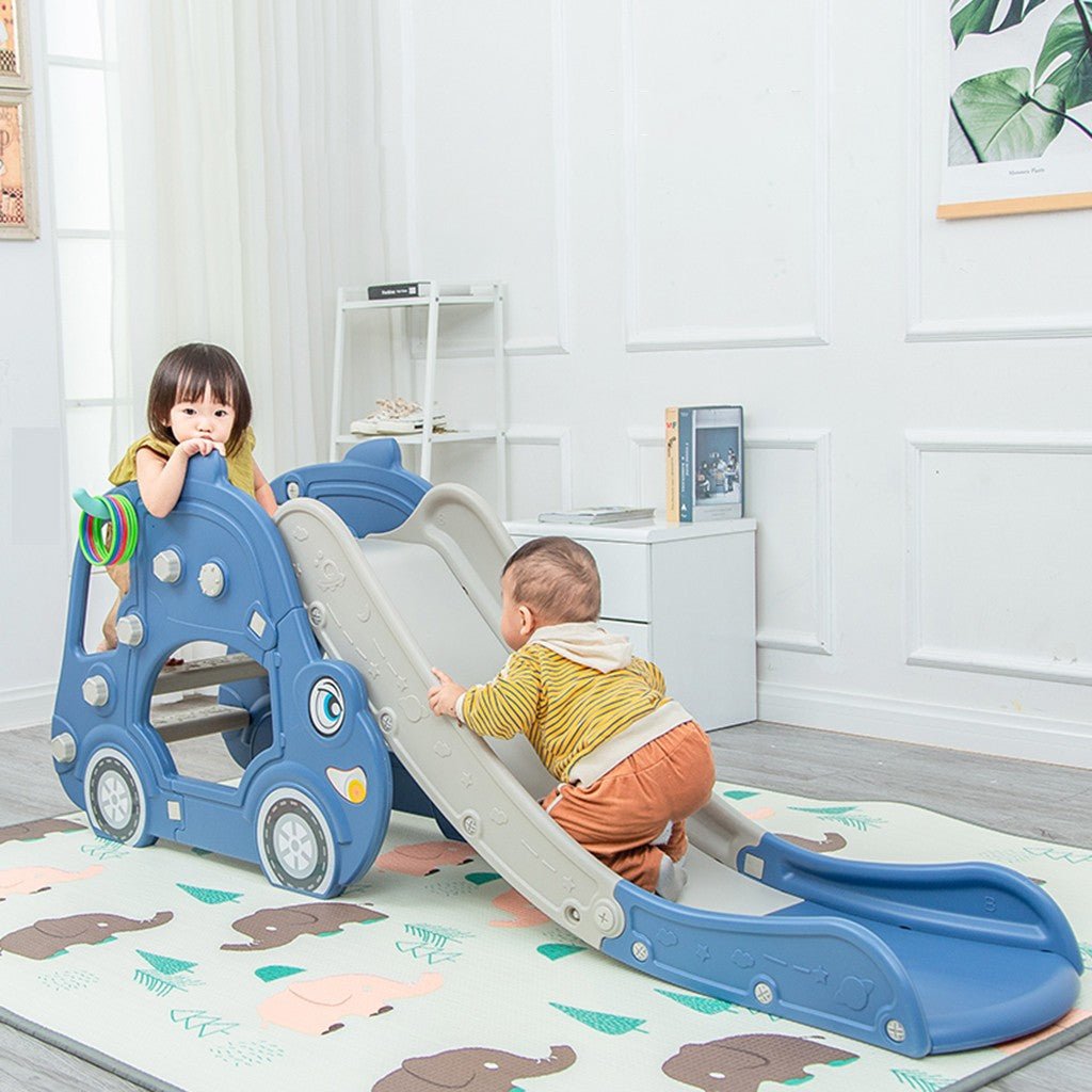 Children playing on a blue and gray slide in a room with a white wall and shelves.
