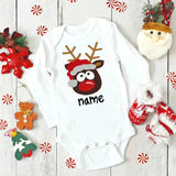 White baby onesie with reindeer design and 'name' text, surrounded by Christmas decorations on a wooden surface.