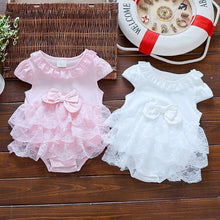 Two baby rompers, one pink and one white, on a wooden surface with a life buoy in the background.