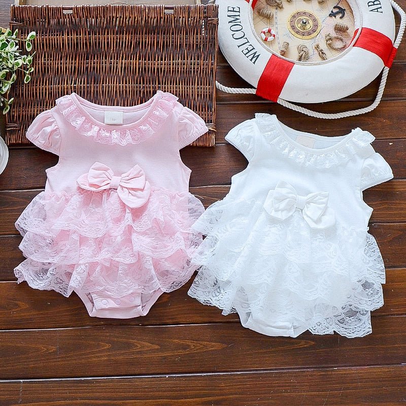 Two baby rompers, one pink and one white, on a wooden surface with a life buoy in the background.