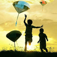 Two children running in a field with toy parachutes against a sunset sky.