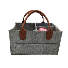 Gray felt storage caddy with brown leather handles used as a nursery diaper basket.