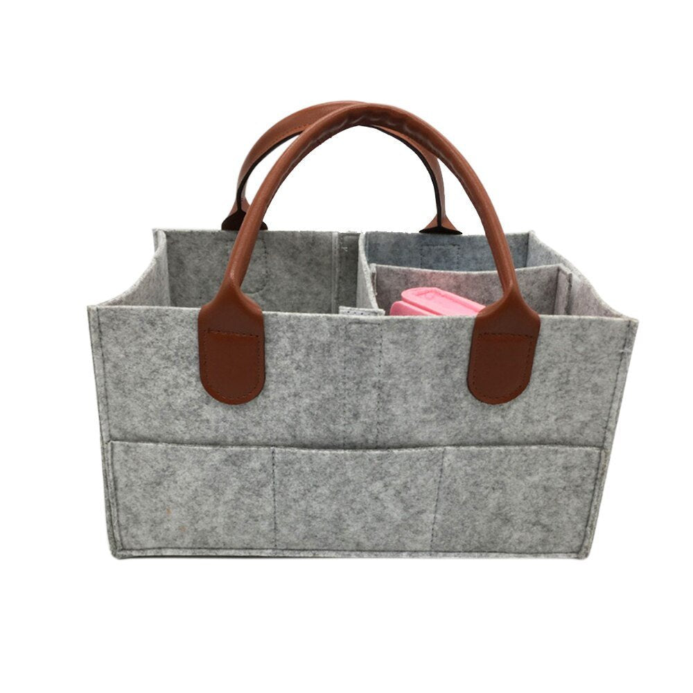 Gray foldable diaper caddy basket with brown leather handles for easy nursery carrying.