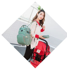 USB Charging Diaper Bag green backpack carried alongside a stroller for convenient outings with mom and dad.