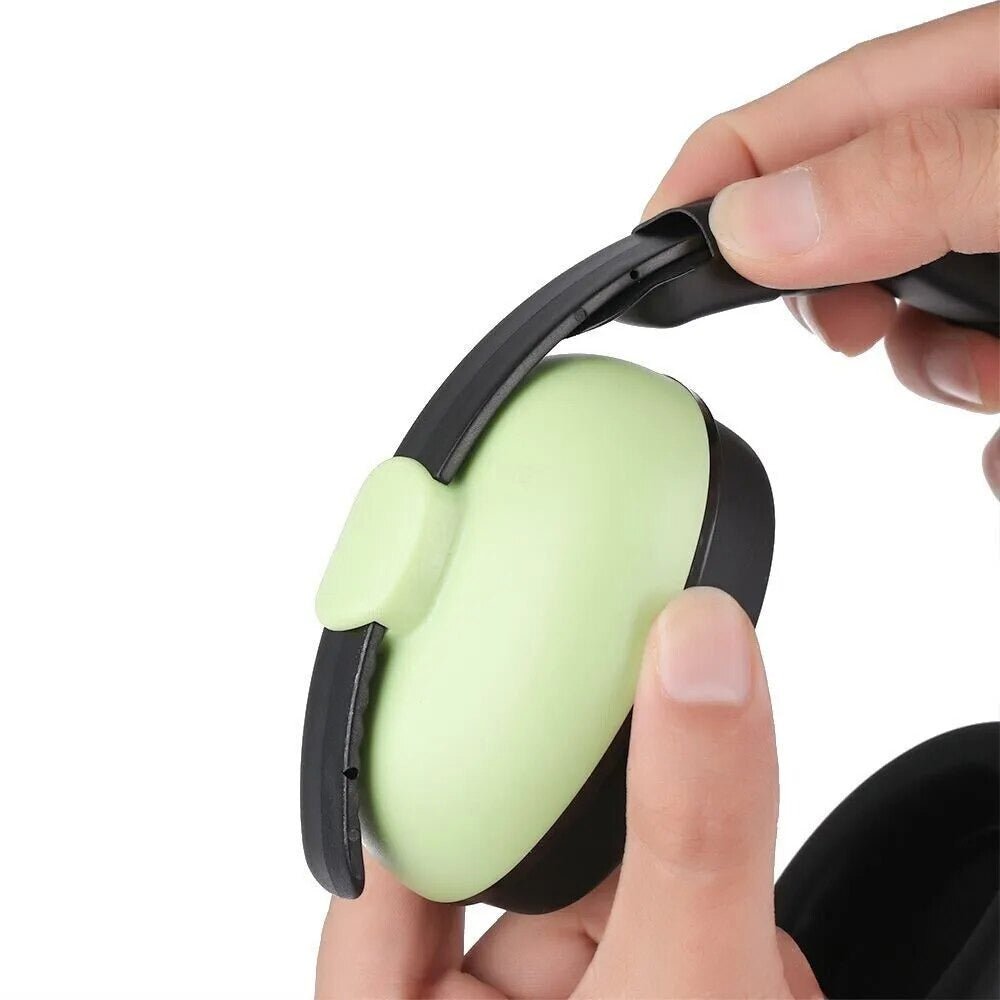 Green infant ear defender held in hand for travel and nap-time noise protection.