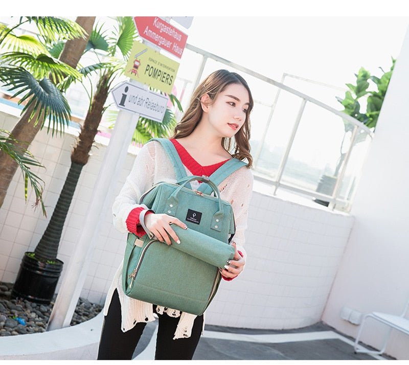 Travel Diaper Bag green backpack with USB charging port for quick access on family outings.