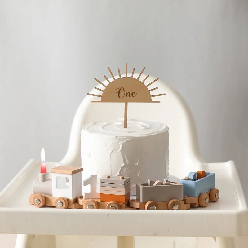 Montessori wooden train and trolley set on a high chair beside a smash cake for toddler birthday photos.