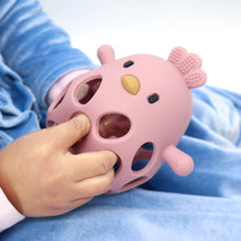 Baby fingers gripping a pink silicone chick teether on a blue blanket
