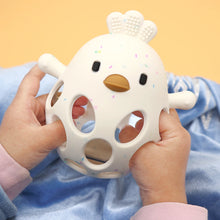 Baby hands holding a white silicone chick teether through its hollow openings