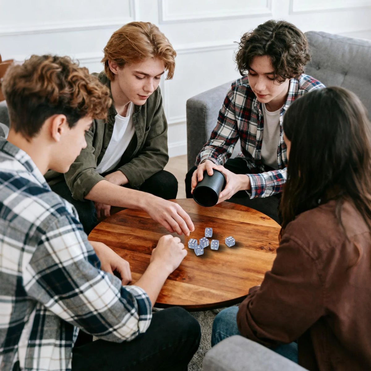 Group of teens and adults rolling dice from a cup at a wooden table