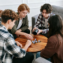 Group of teens and adults rolling dice from a cup at a wooden table