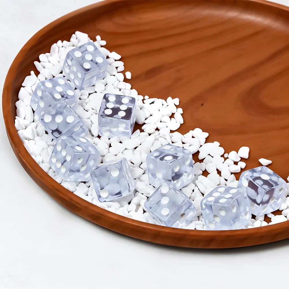 Transparent white-dot dice in a wooden dish with small white stones