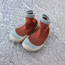 Pair of orange knit baby boots with light blue trim on a glittery silver background