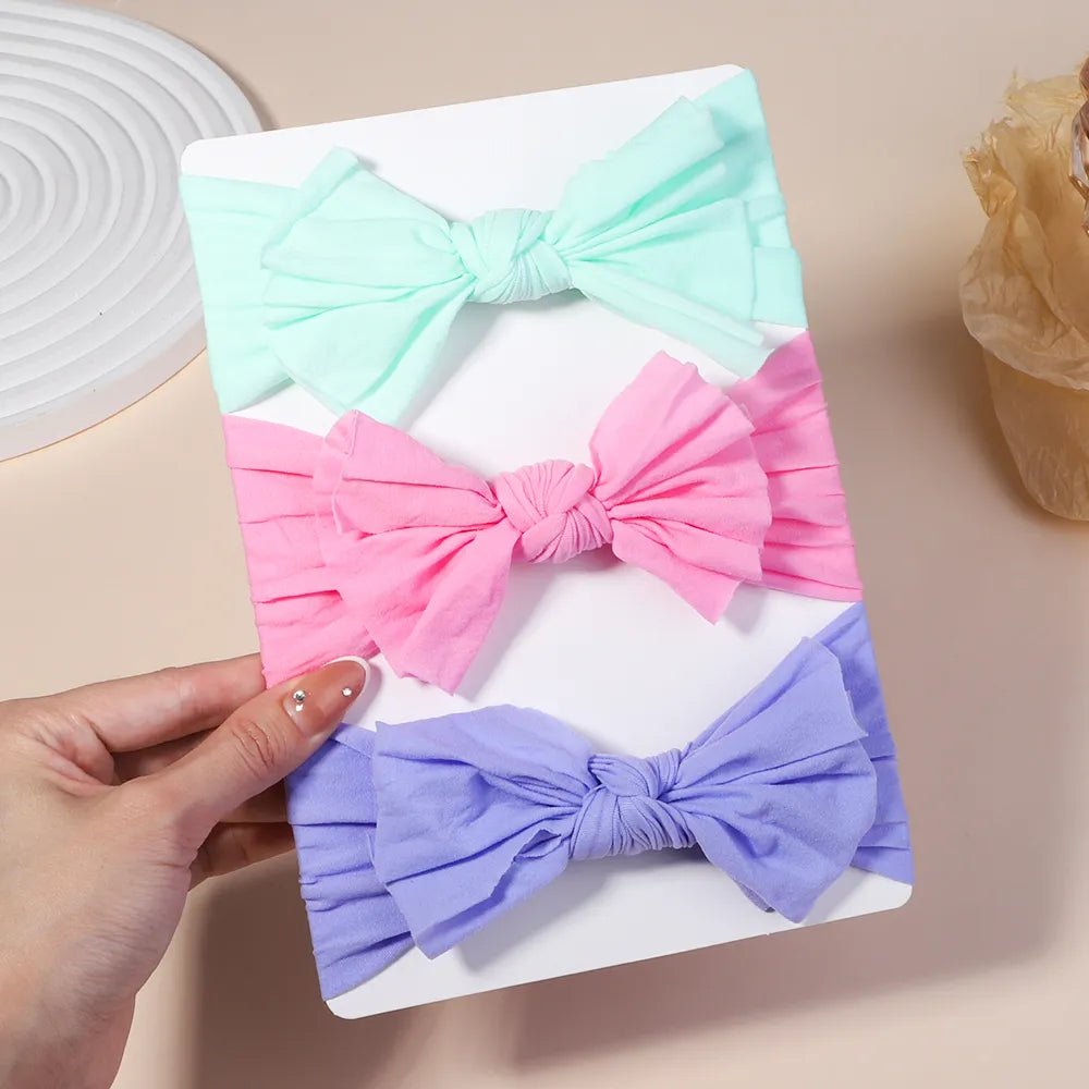 Three colorful hair bows on a white card held by a hand 