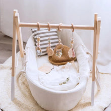 White baby crib with wooden frame, striped pillow, and hanging toys on a light wooden floor.