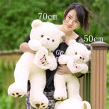 Person holding two white teddy bears with size labels outdoors