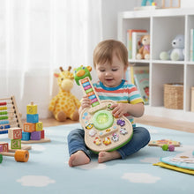 Toddler sitting on a play rug holding a green giraffe toy guitar with toys behind