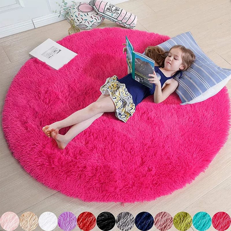 Child reading a book on a large pink round rug in a room.