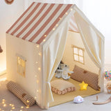 Children's play tent with striped roof, toys, and decorative lights in a room.
