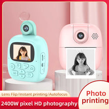 Teal and pink kids instant print cameras with callouts for lens flip, instant printing and autofocus