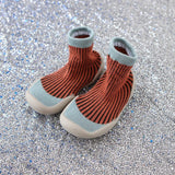 Pair of orange knit baby boots with light blue trim on a glittery silver background