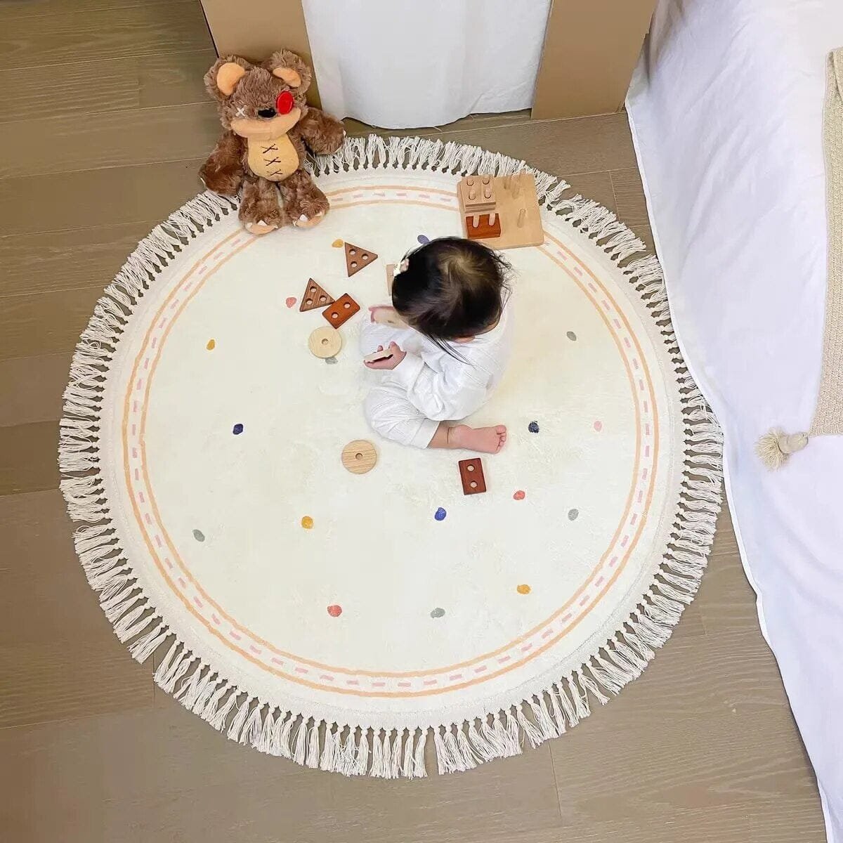 Baby playing on a round white rug with toys on a wooden floor.