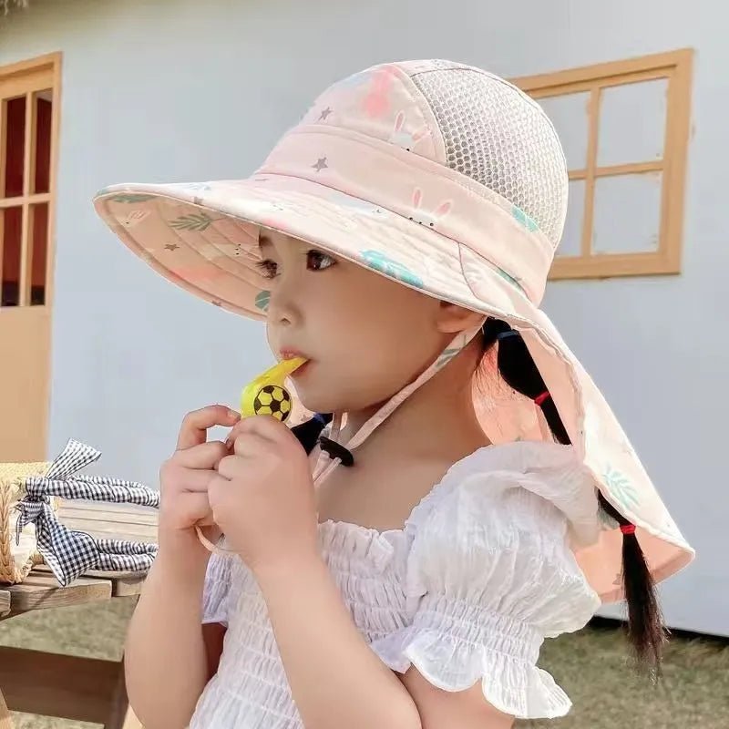 Child wearing a pink sun hat with a mesh design, eating a lollipop outdoors.