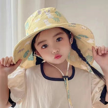 Child wearing a yellow patterned sun hat indoors