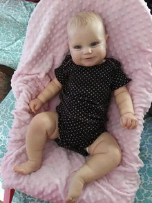 Maddie Reborn Doll, baby doll in a black polka dot outfit lying on a pink cushion, for baby shower and holiday gifting.