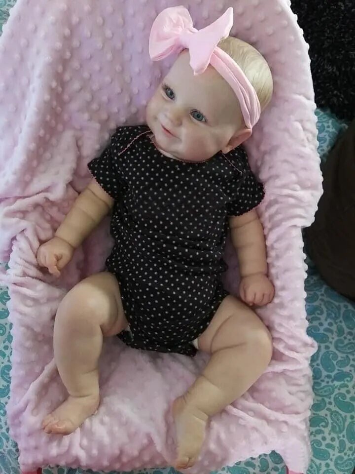 Maddie Reborn Doll, baby doll in a black polka dot outfit with a pink bow on a pink blanket, for realistic play and cuddling.