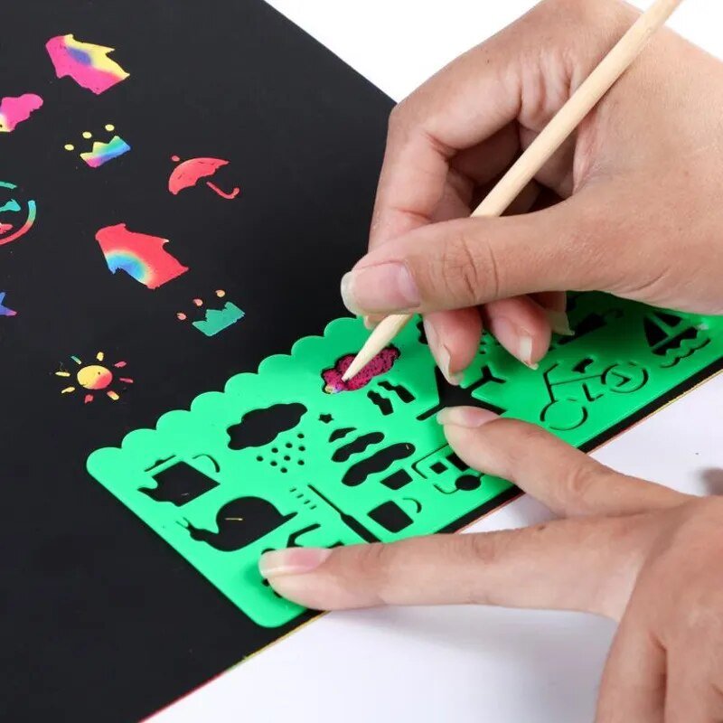 Magic Rainbow Scratch Art Card Set, a person using a green stenciling tool to color on black paper, for classroom art and craft projects.