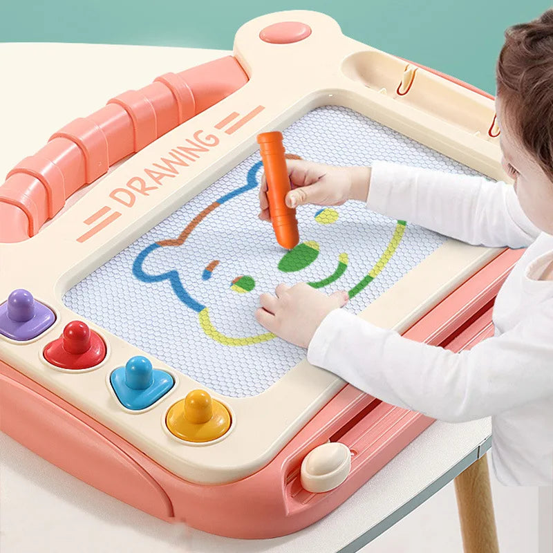 Child drawing a bear with an orange pen on a pink magnetic drawing board with colorful stamps