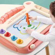 Child drawing a bear with an orange pen on a pink magnetic drawing board with colorful stamps