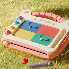 Pink magnetic drawing board on grass with four colored blocks pressed onto the screen