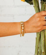 A hand wearing gold bracelets holding a plant.