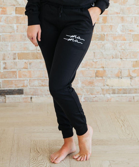 Person wearing black jogger pants with white text.