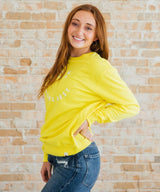 Woman wearing a yellow sweatshirt with text against a brick wall