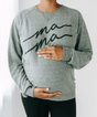 Person wearing a gray sweatshirt with 'ma ma' text, holding their pregnant belly.