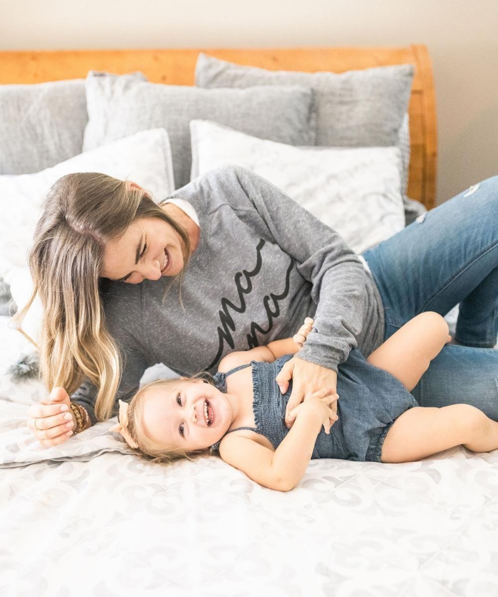 Woman and child lying on a bed together, smiling.