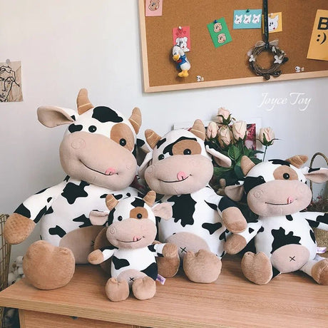 Four cow-themed plush toys on a wooden surface.