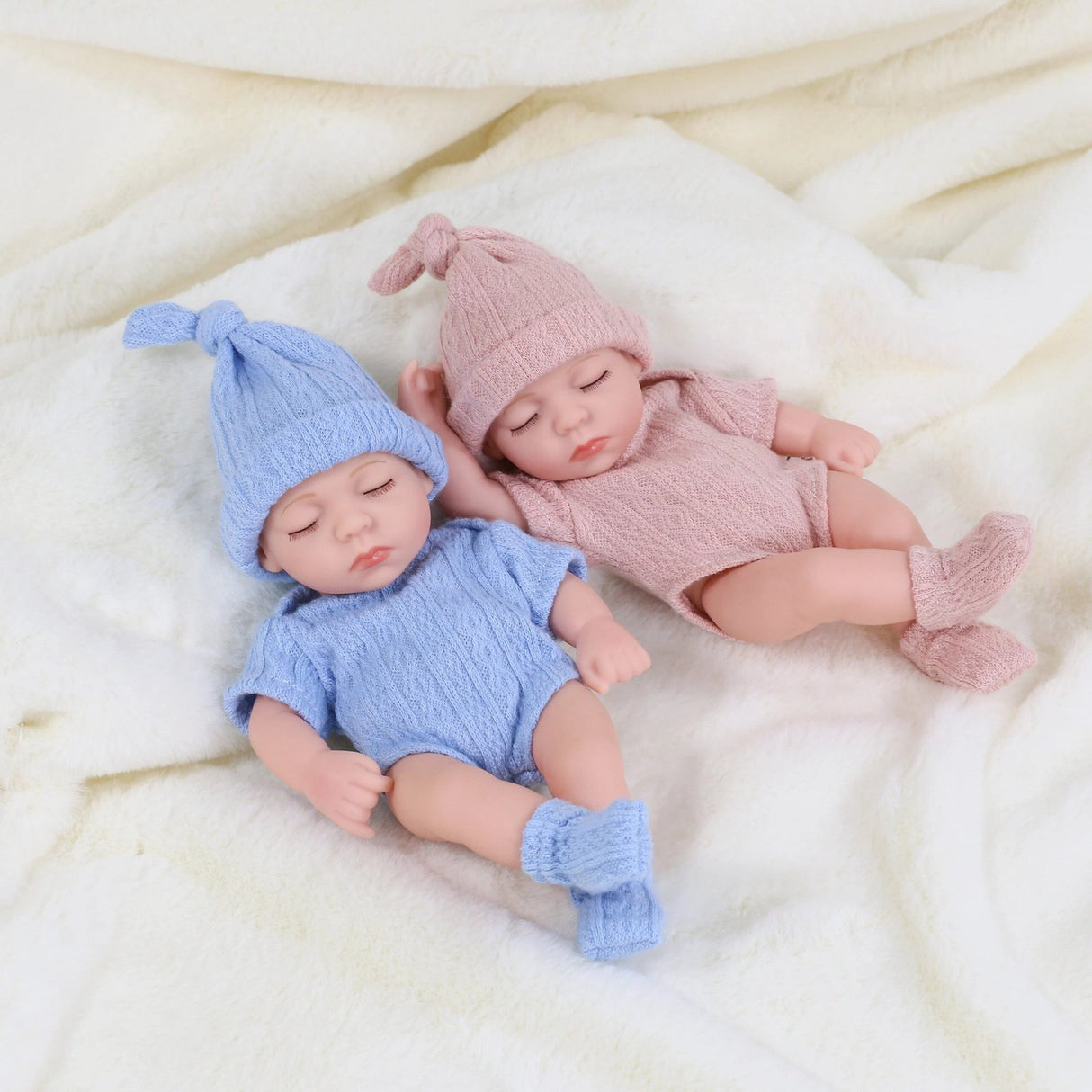 Two baby dolls in blue and pink outfits lying on a soft surface.